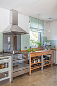 Stainless steel cooker with extractor hood next to wooden, open-fronted kitchen counter