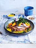A slice of bread topped with soused herring, orange and butter sauce and a wild herb salad