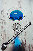 Glass of vivid blue cocktail and twisted spoon on rustic table