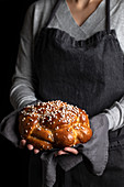 Crop housewife in apron holding appetizing tasty homemade braid bread with sprinkles