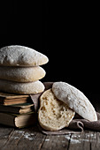 Pile of freshly baked tasty homemade bread placed on wooden table next to cut piece against black background