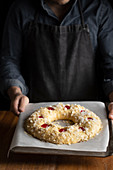 Crop chef in black apron holding unbaked round bread topped with cherry while standing at wooden table