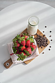 Ripe strawberries and heap of chocolate pellets on cutting board near bottle of milk