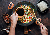 Pouring soy sauce into pan with chopped chicken and vegetables while preparing delicious noodles