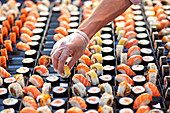 Anonymous salesman in protective gloves putting in sushi in plastic container on market