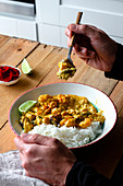 Taking piece of spicy curry made of prawns and mushrooms and served with rice and lime slices