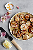 Slices aromatic garlic on caps of raw Shiitake mushrooms in deep ceramic oven tray