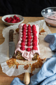 Sweet homemade cake topped with whipped cream and garnished with fresh raspberries on baking paper