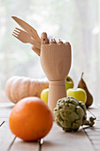 Holzhand mit Gabel und Messer auf Tisch zwischen Obst und Gemüse