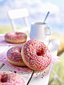 Donuts mit rosa Zuckerglasur und bunten Streuseln auf Gartentisch