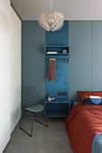 Blick auf blaues Garderobenpaneel als Nachttisch neben Bett und Drahtstuhl