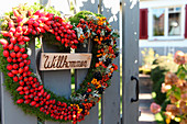 Welcome wreath on garden gate made from moss heart with rosehips, rowan berries and pyracantha berries
