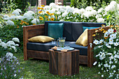 Sofa im Garten zum draußen wohnen im Sommer, umgeben von Strauchhortensien, Sonnenhut und Schmuckkörbchen