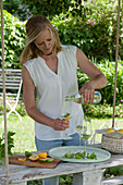Frau füllt Gläser mit Mineralwasser, frische Minze und Orangenscheibe, Orange und Limette