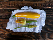 Fresh yellow zucchini and zucchini flowers on a linen cloth