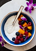 Vanilla yoghurt with mango, raspberries, blueberries and an edible flower garnish (purple orchid)