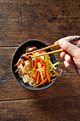 Hands taking Chinese vegetable and duck stir fry with chopsticks