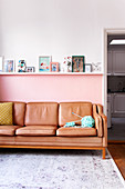 Ledersofa vor rosa Wand, darüber Regal mit Fotos und Bildern