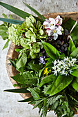 A spring flower arrangement in a wooden bowl with wild garlic, dandelions, fruit blossom and beech twigs