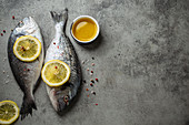 Raw fresh fish dorado with lemon wedges, olive oil and seasonings