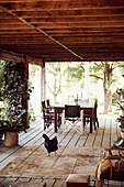 Wooden terrace with dining table and chairs, in the foreground a rooster