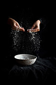 Flour being sprinkled from hands on a dark background
