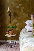 Metal bedside table next to bed in bedroom with patterned wallpaper