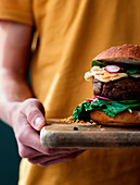 Hand holding delicious vegan lentils hamburgers placed on wooden board