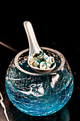 High angle of spoon with small seashells placed on crackled vase with blue cocktail