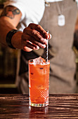 Barkeeper steckt Trinkhalm in Cocktailglas