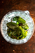 Top view of glass cup with heap of fresh mint leaves placed on table in bar