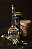 Bunch of fresh herbs placed on table near bottle of vinegar and jars with spices on black background