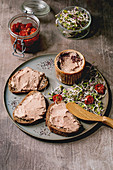 Sandwiches and ceramic bowl of homemade chicken liver pate with wooden knife, sun-dried tomatoes and green sprout salad