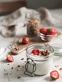 Fermented probiotic kefir or yogurt in glass jar served granola and fresh strawberries