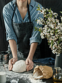 Young woman in blue shirt and gray apron making bread dough