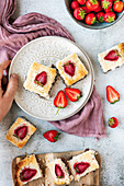 A hand holding a white plate with two slices of coconut ice squares with chocolate bottom and strawberry topping