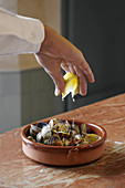 Faceless person in white shirt squeezing lemon slice over bowl of delicious freshly cooked mussels