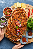 Woman holding a wooden board with Turkish lahmacun with red onion salad and tomato salad as condiments