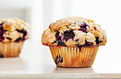 A close, detail image of a rustic, blueberry muffin on a white tabletop