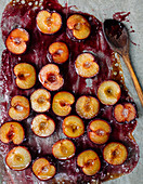 Oven-baked plums on baking paper with a wooden spoon