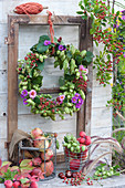 Autumn wreaths made of hops, asters and rose hips hung on old window frames, wire baskets with apples