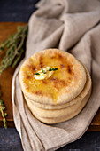 A stack of Turkish flatbread called bazlama topped with butter and thyme on a wooden board.