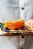 Woman holding a honey comb accompanied by lavenders on a wooden board.