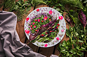 Creative composition of delicate flowers and delicious green herbs placed on wooden table with napkin