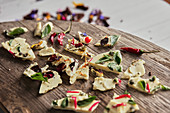 Pieces of tasty chocolate with various flower petals and herbs placed on wooden table