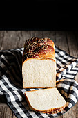Loaf of fresh bread with sesame placed on cloth cutting board in kitchen on black background