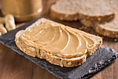 Piece of bread with peanut butter placed on black slate broad on wooden table with knife and fork