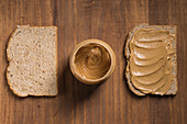 Bread slices with creamy peanut butter placed on wooden table in kitchen with jar