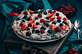 Delectable sweet meringue Pavlova cake with assorted fresh berries including strawberry and raspberry with cherry and blueberry