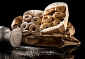 Cardboard boxes filled with round baked doughnuts in nuts and icing sugar on table
